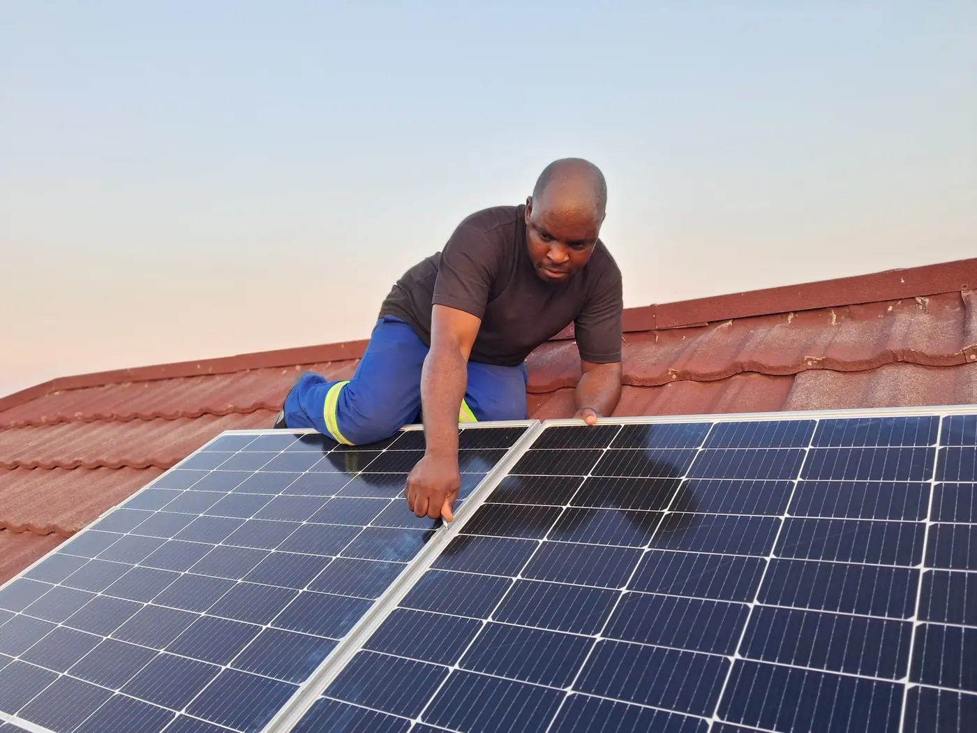 Technician aligning solar panels on a tiled roof at sunset