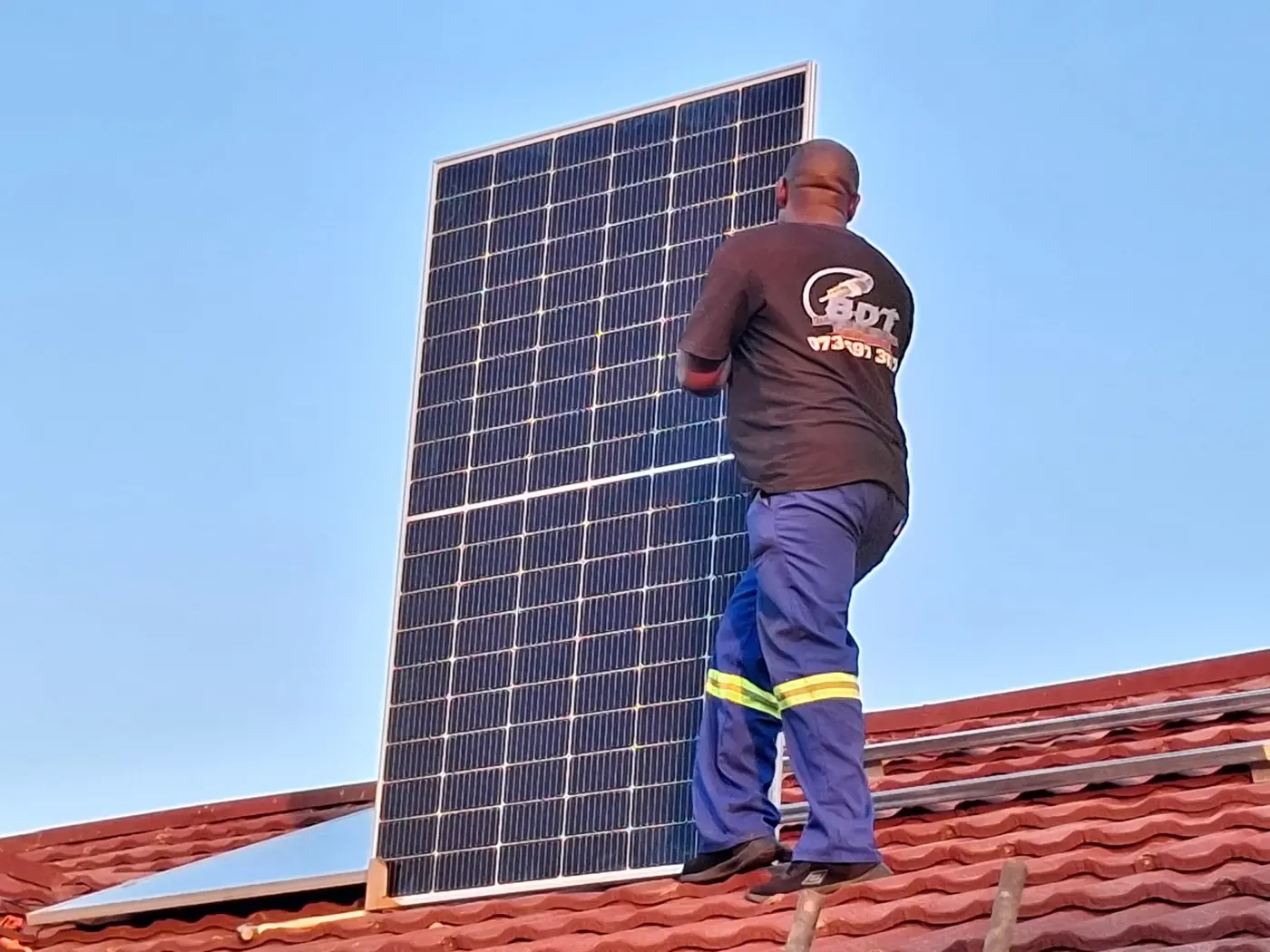 Technician lifting a solar panel into position on a roof